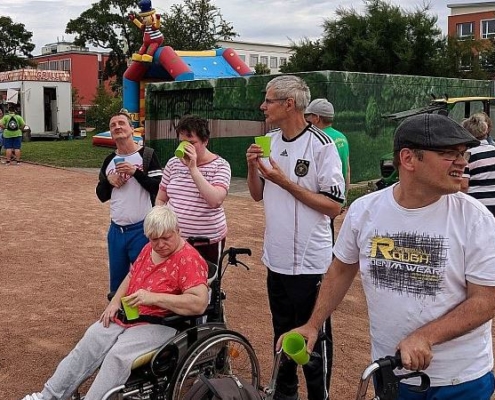 Die Sportler stehen am Rand und trinken aus grünen Bechern.