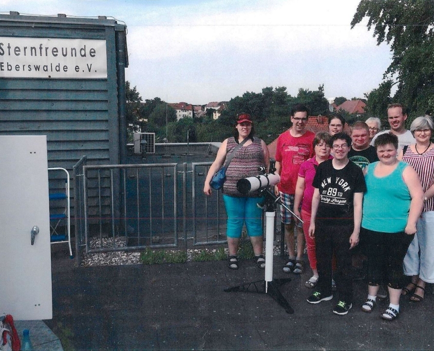 Auf de Dach der Sellheim-Schule hat sich der Deutschkurs vor der Sternwarte zum Gruppenfoto aufgestellt. Vor den sechs Frauen und vier Männern steht ein Fernrohr. Im Hintergrund sind Bäume und mehrere Hausdächer zu sehen.