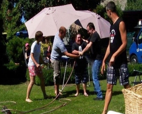 Mehrere Personen versuchen sich auf dem Rasen gegenseitig mit dem Wasserschlauch zu bespritzen.