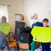 Im Vordergrund halten Frau Bester und ein jugendlicher Bewohner je ein apfelgrünes Handtuch in den Händen. Dahinter zeigt Frau Bollgehn ein anthrazitfarbenes.