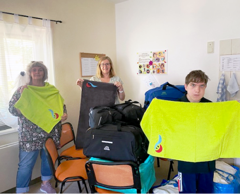 Im Vordergrund halten Frau Bester und ein jugendlicher Bewohner je ein apfelgrünes Handtuch in den Händen. Dahinter zeigt Frau Bollgehn ein anthrazitfarbenes.