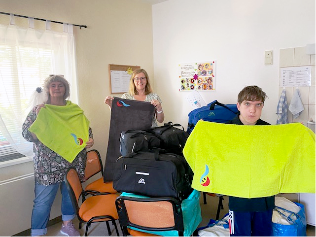 Heidehaus_Spende_Handtücher: Abtrocknen in Apfelgrün und Anthrazit. Im Vordergrund halten Frau Bester und ein jugendlicher Bewohner je ein apfelgrünes Handtuch in den Händen. Dahinter zeigt Frau Bollgehn ein anthrazitfarbenes.