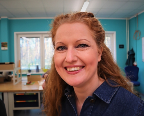 Im Porträt ist die Gruppenleiterin Steffi Wilke zu sehen. Sie lacht in die Kamera, hat lange , rötliche Haare und eine dunkelblaue Jeansbluse an.