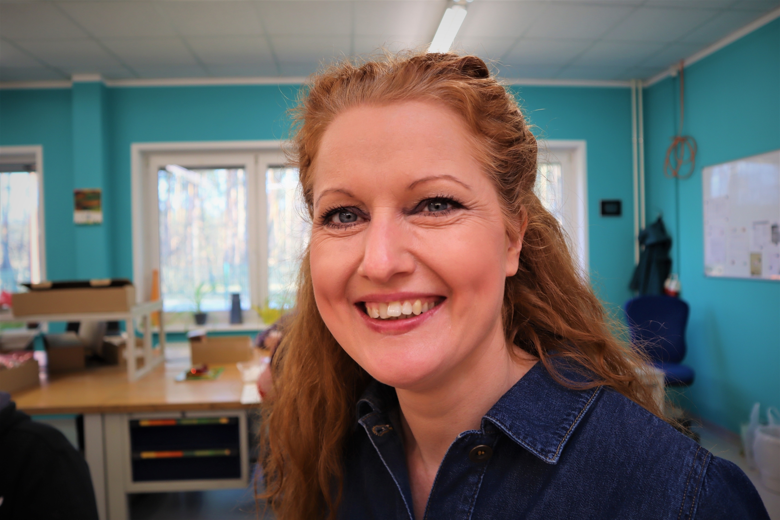 Gruppenleiterin Steffi Wilke - immer gut gelaunt Im Porträt ist die Gruppenleiterin Steffi Wilke zu sehen. Sie lacht in die Kamera, hat lange , rötliche Haare und eine dunkelblaue Jeansbluse an.