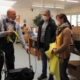 Frau Wiese und Herr Gloger sprechen in der Abteilung Montage mit dem Vorsitzenden des Werkstattrates. Dieser hält konfektionierte gelbe Kabel in seiner rechten Hand. Er stützt sich auf einen Rollator. Im Hintergrund sind andere Beschäftigte an ihren Arbeitsplätzen zu sehen.