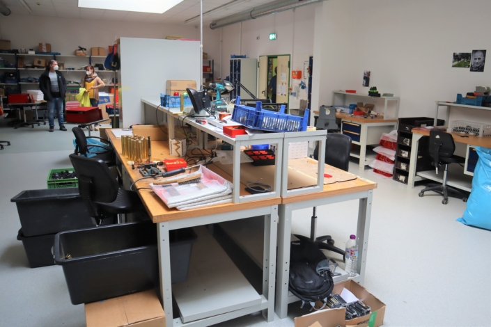 In der Mitte stehen Werkstatttische mit Aufsatz. Darauf liegen verschiedene Arbeitsutensilien. An der rechten Wand stehen zwei weitere Arbeitstische mit Aufsatz.