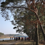 Das Bild wurde von der anderen Seite, aus größerer Entfernung aufgenommen. Die Sportlerinnen erwärmen sich mit verschiedenen Übungen,. Einige recken die Arme in die Luft. Im Hintergrund ist die blau-gelbe Kanalbrücke zu erkennbar.