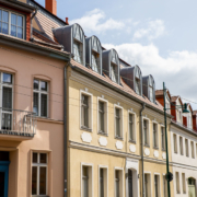 Die Putz-Fassade der Breite Straße 54 ist beige gestrichen. Das Haus besteht aus Erd-, Ober- und Dachgeschoss mit Gauben. Der Fußweg ist durch Poller mit Ketten von der Straße getrennt.