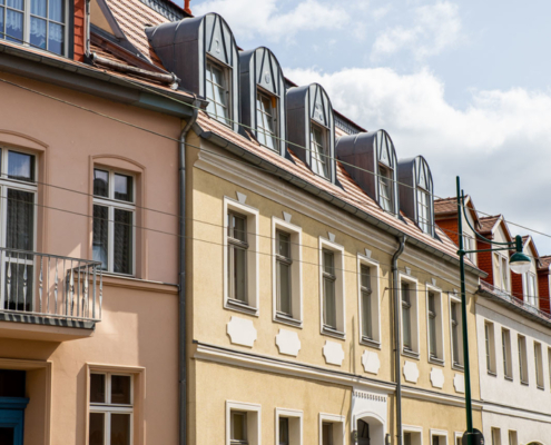 Die Putz-Fassade der Breite Straße 54 ist beige gestrichen. Das Haus besteht aus Erd-, Ober- und Dachgeschoss mit Gauben. Der Fußweg ist durch Poller mit Ketten von der Straße getrennt.