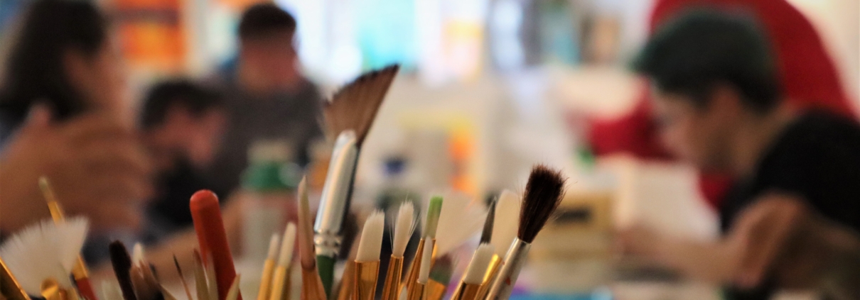 Den Vordergrund des Fotos bilden Pinsel in verschiedenen Größen. Der Rest des Raumes ist mit Abicht unscharf aufgenommen.