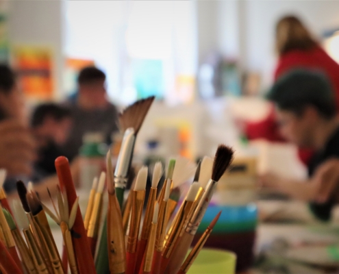 Den Vordergrund des Fotos bilden Pinsel in verschiedenen Größen. Der Rest des Raumes ist mit Abicht unscharf aufgenommen.