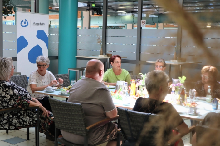 Ein Mann unter Frauen Der Mann sitzt zwischen zwei Frauen mit den Rücken zur Kamera. Gegenüber fällt der Blick auf vier Frauen vor der Trennwand zum Schwimmbad.