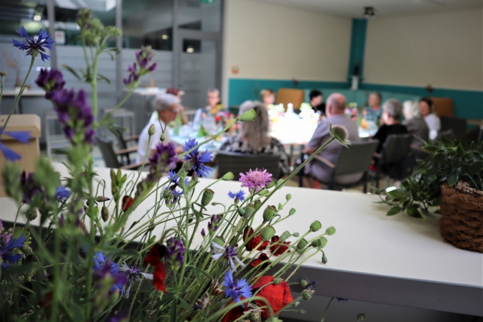 durch die Blume Über einen bunten Blumenstrauß hinweg fällt der Blick auf die Runde der ehrenamtlich Tätigen. Dabei steht der Blumenstrauß im Fokus.